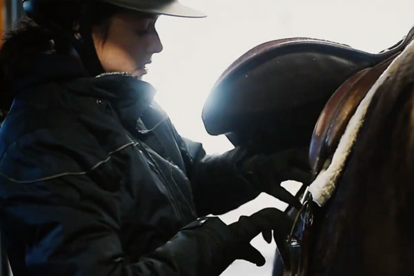 a close up of a girl adjusting a horse saddle