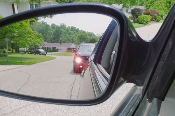 a car's side mirror showing a car behind it tailgating