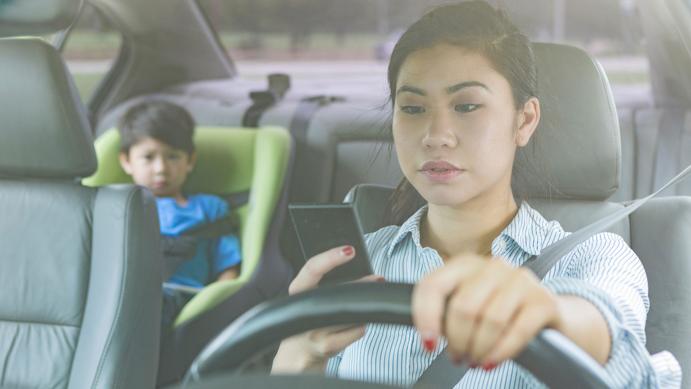 mother driving and looking at her phone with her child in the back seat