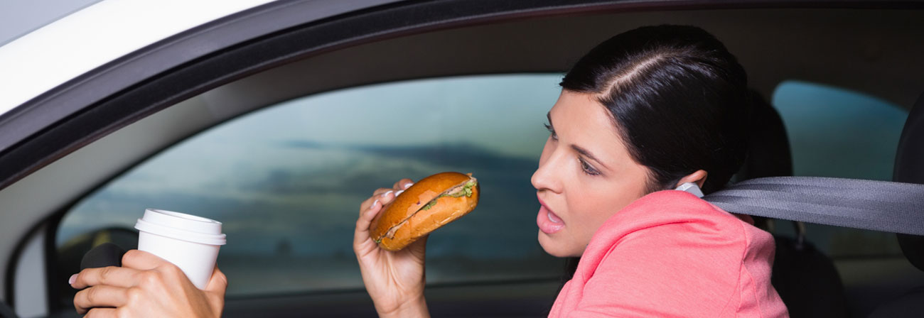 woman driving, eating her breakfast, holding a cup of coffee and talking on her cell phone