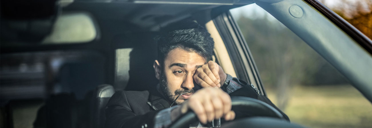 a man driving rubbing his eyes