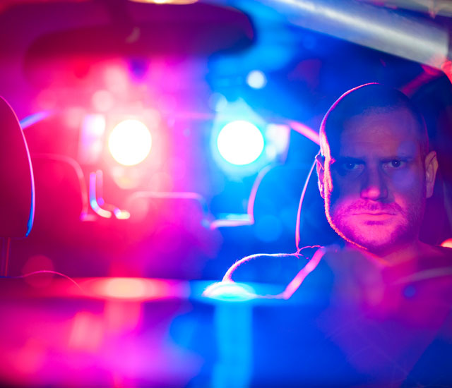 an angry man behind the wheel with police lights shining through the car