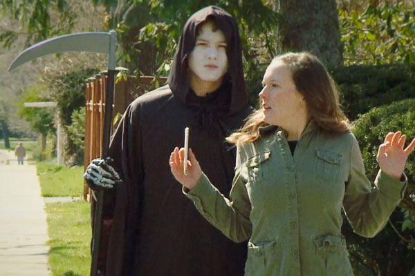 the grim reaper standing behind a woman holding a cell phone